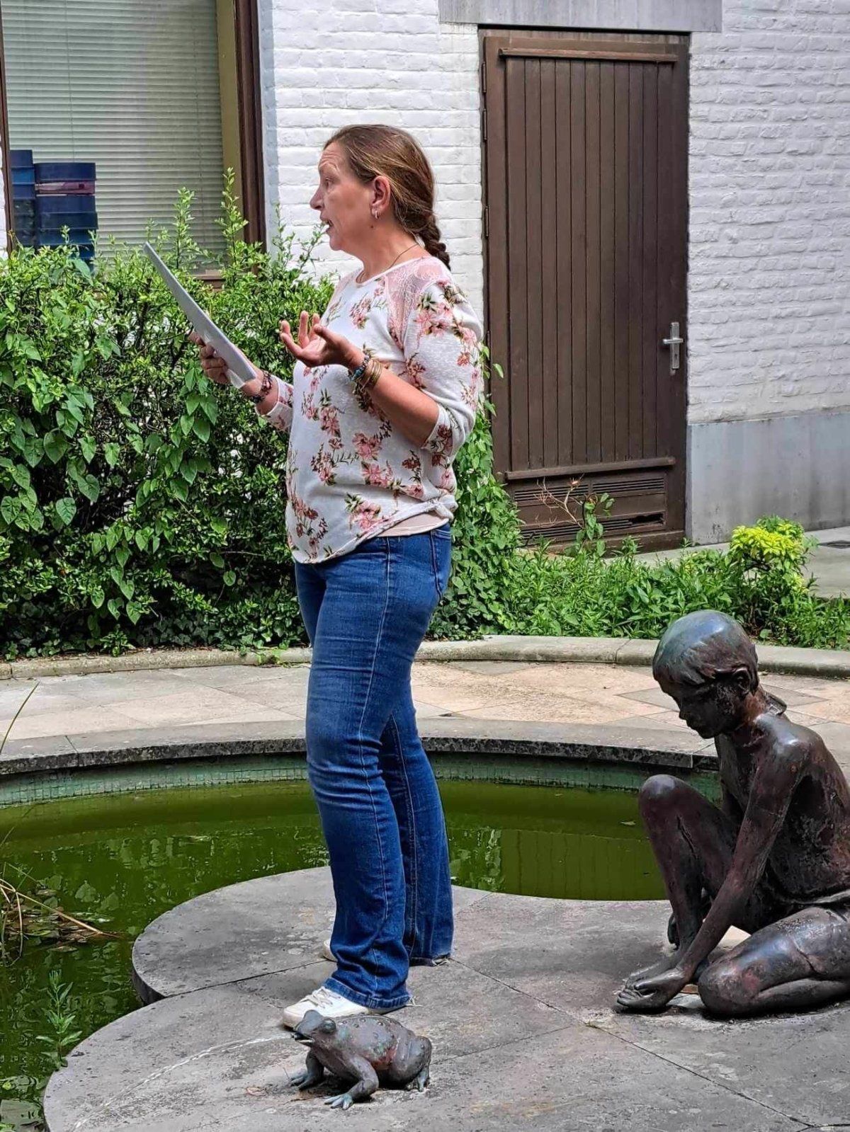 Lecture vivante Lemokili une personne en rain de lire un texte dans un décor avec un petit étang et une statuette de petite fille